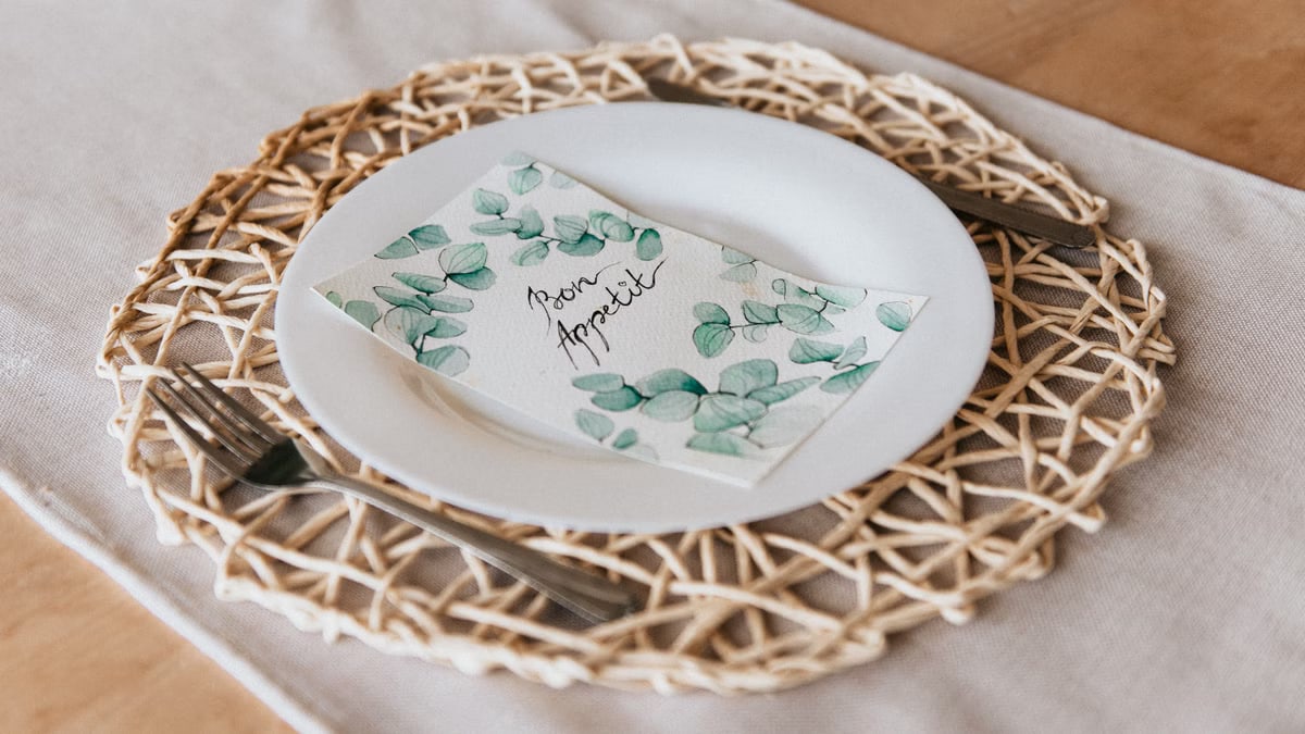 Stylish table setting with a woven placemat and 'bon appetit' napkin on a white plate.